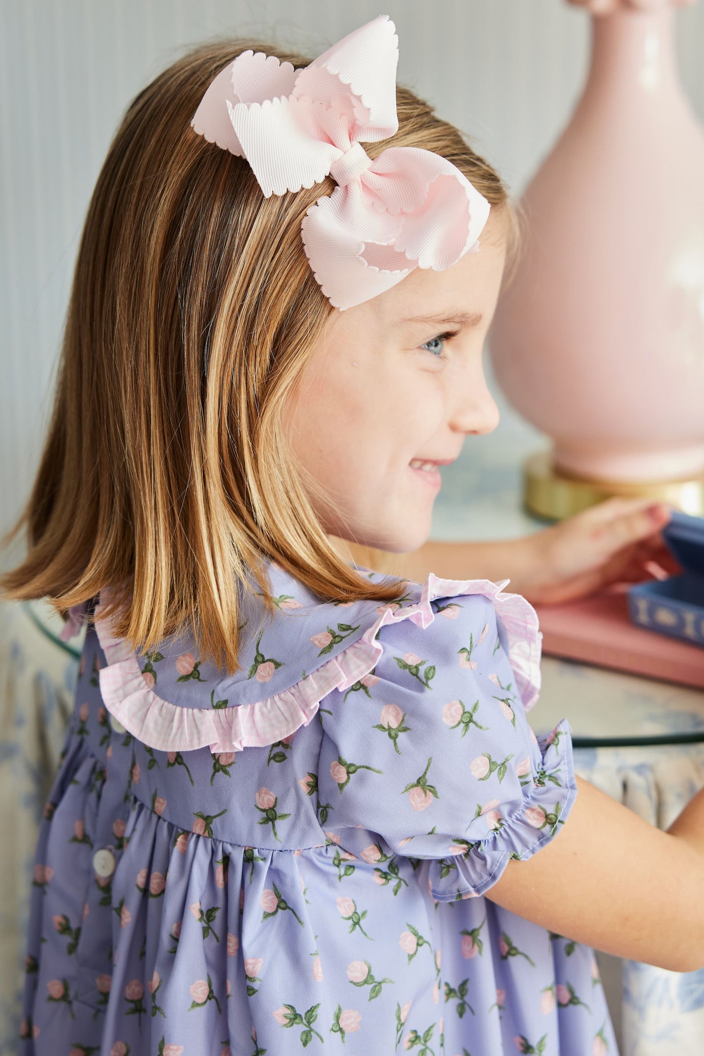 Young girl wearing a floral dress with a large pink bow in her hair.