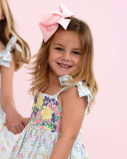 Young girl wearing a floral dress with a large pink bow in her hair against a pink background