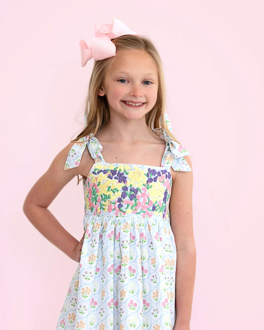 Young girl wearing a floral dress with a pink bow on a light pink background