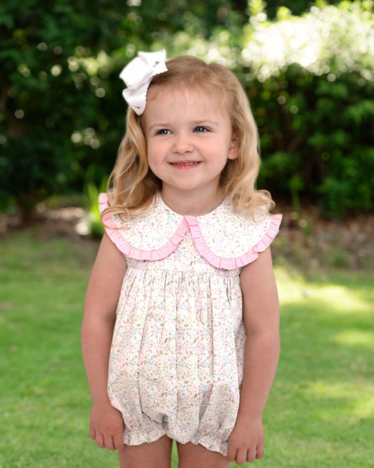 Young girl wearing a floral dress with a pink collar outdoors.