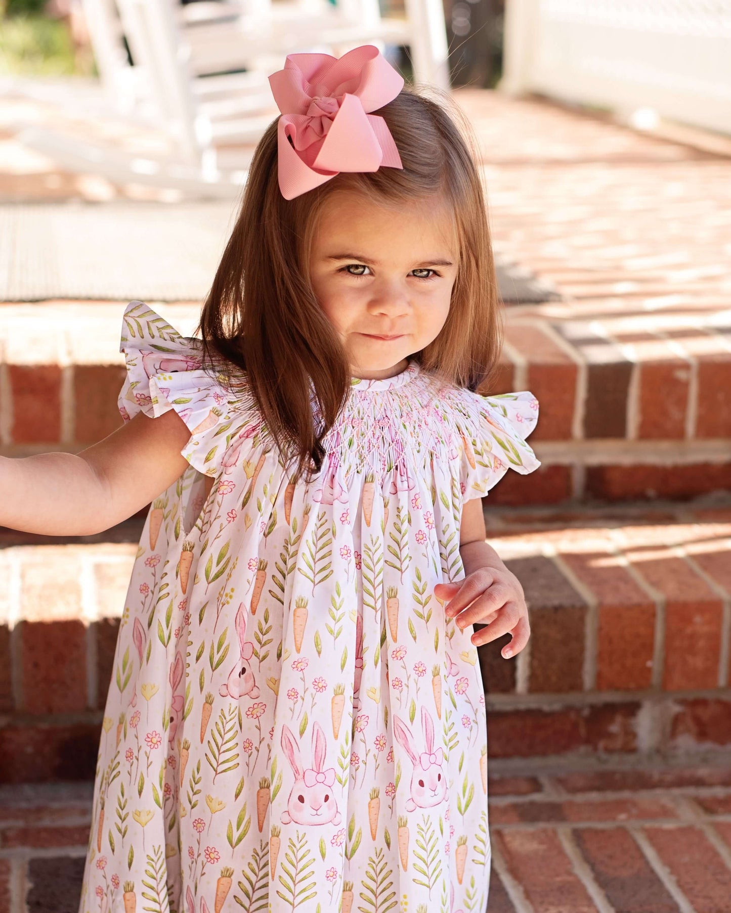 Young girl wearing a floral dress with bunny designs, standing on a brick step.