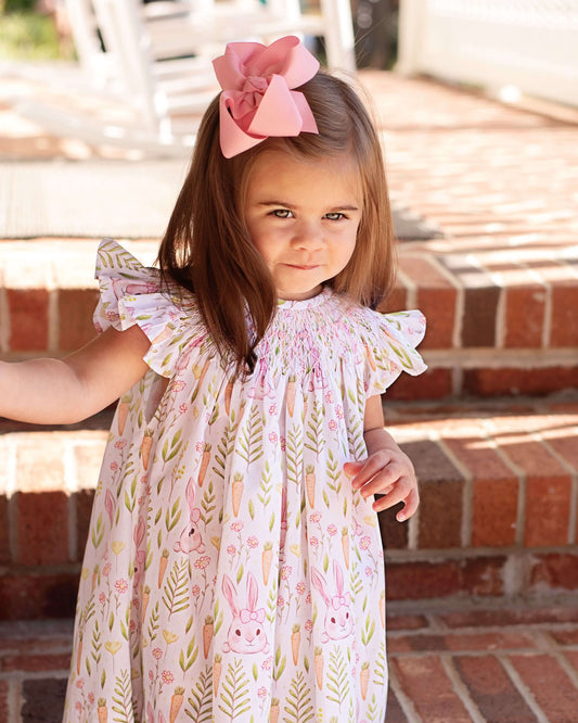 Young girl wearing a floral dress with bunny designs, standing on a brick step.