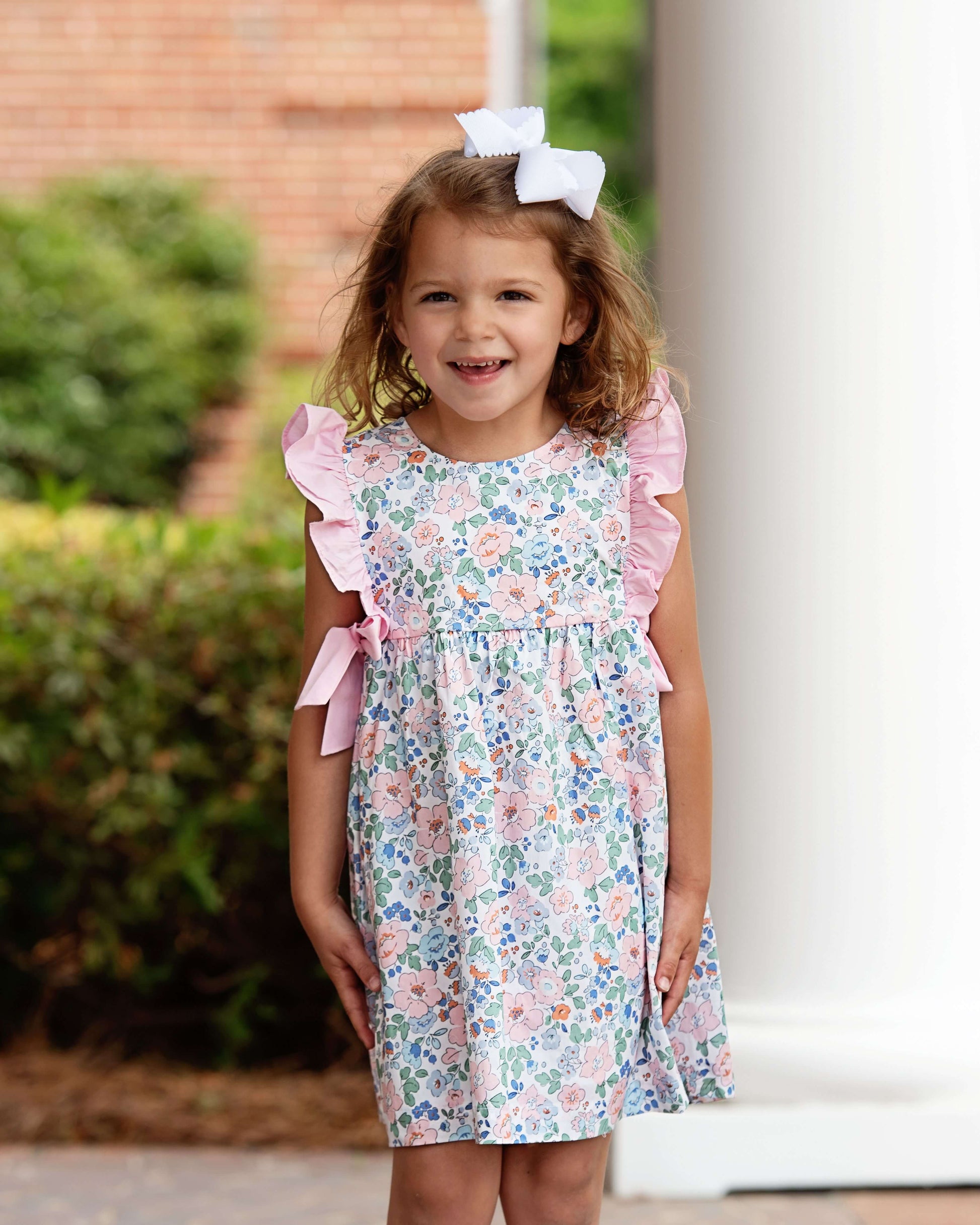 Young girl wearing a floral dress with pink ruffles outdoors.