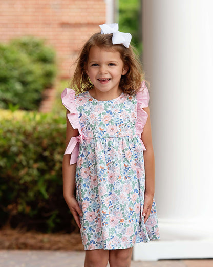 Young girl wearing a floral dress with pink ruffles outdoors.