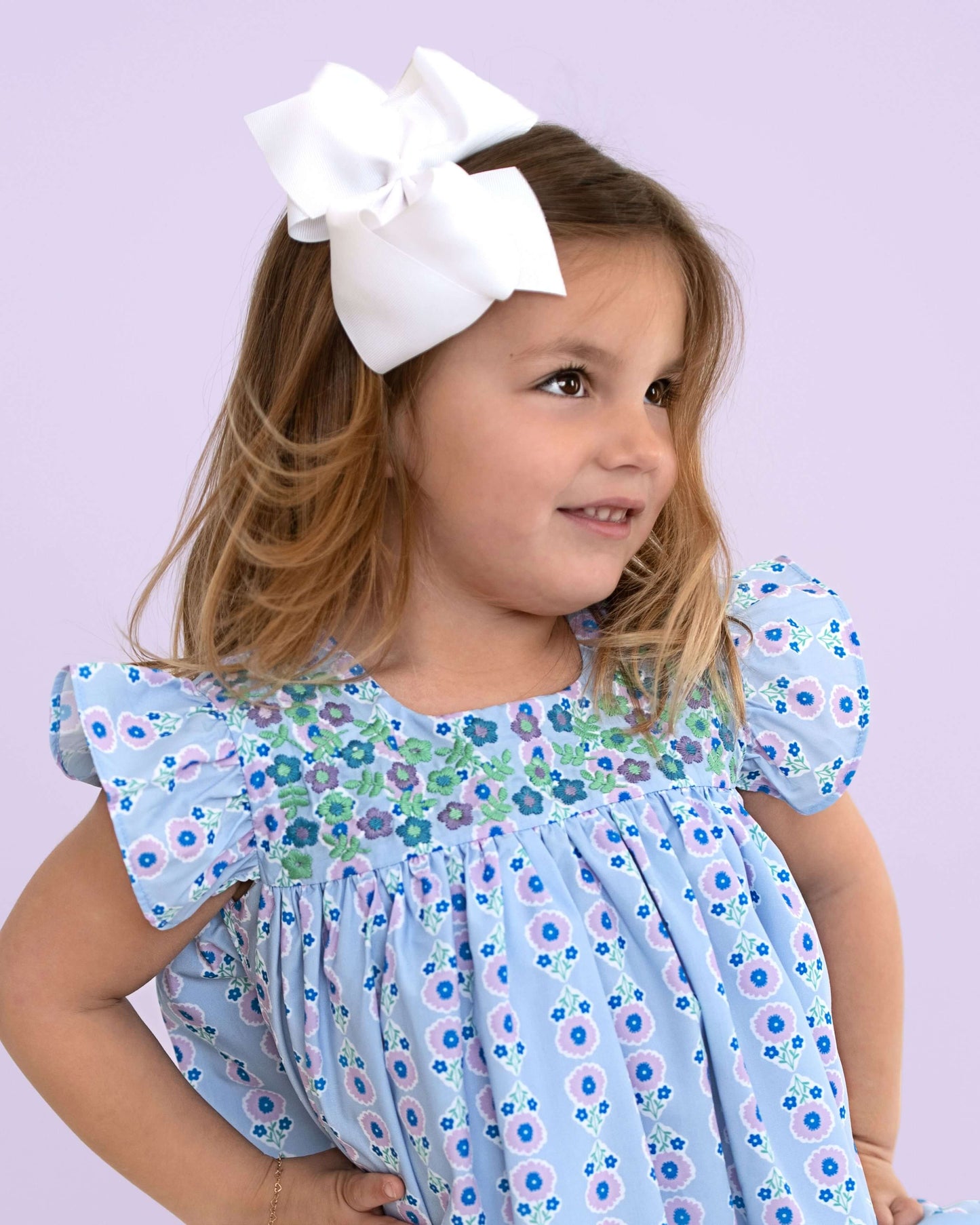 Young girl wearing a floral dress with puffed sleeves against a light purple background