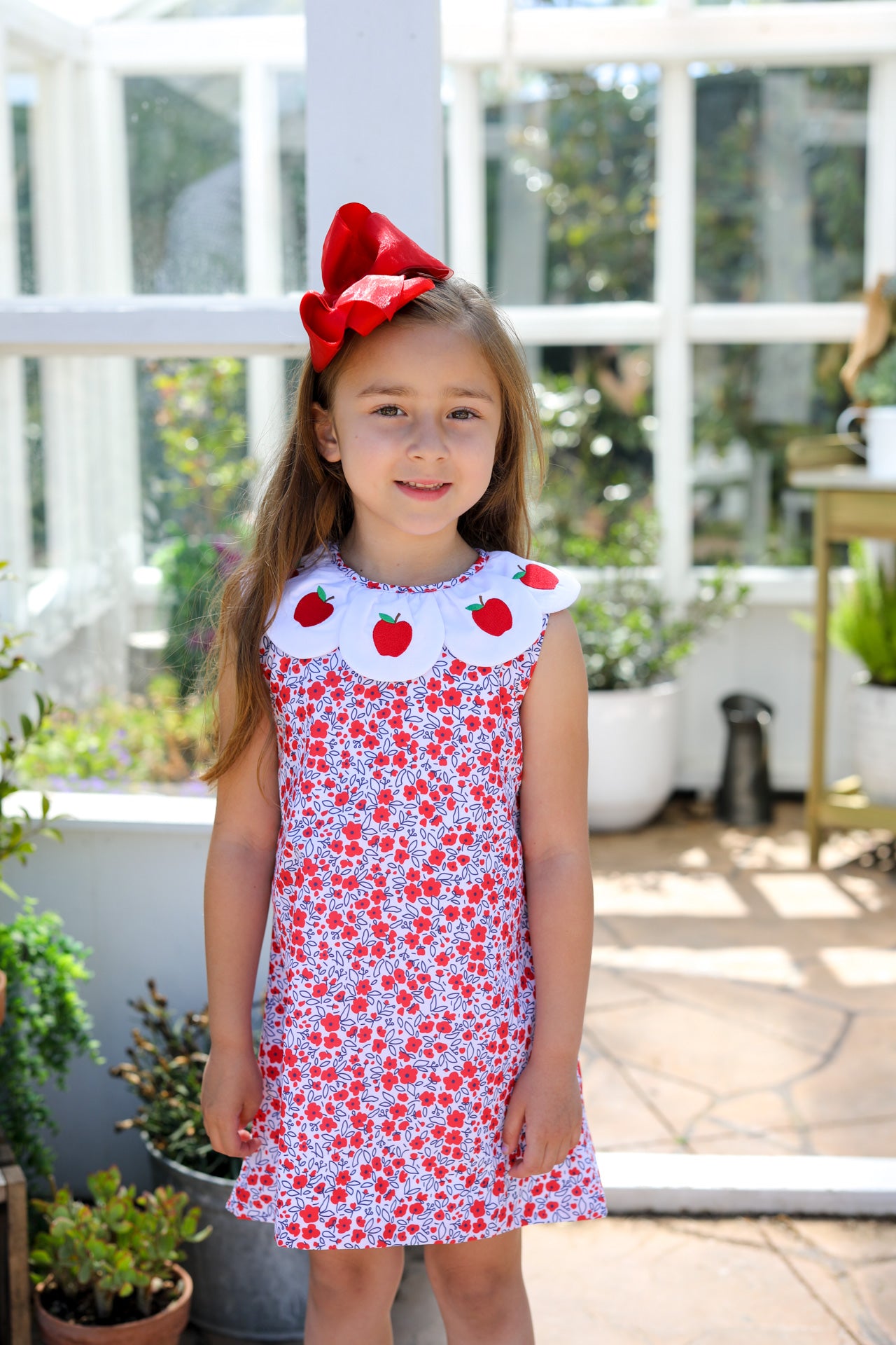 Young girl wearing a floral dress with scalloped collar wearing apples.