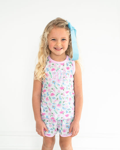 Young girl wearing a floral romper with a blue bow in her hair on a white background