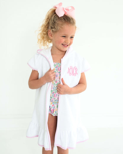Young girl wearing a floral swimsuit with a white cover-up and pink hair bow on a white background