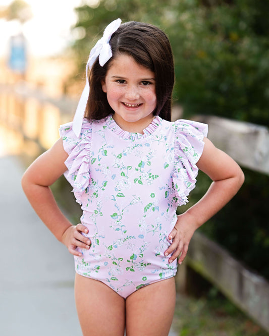 Young girl wearing a floral swimsuit with ruffled sleeves outdoors.
