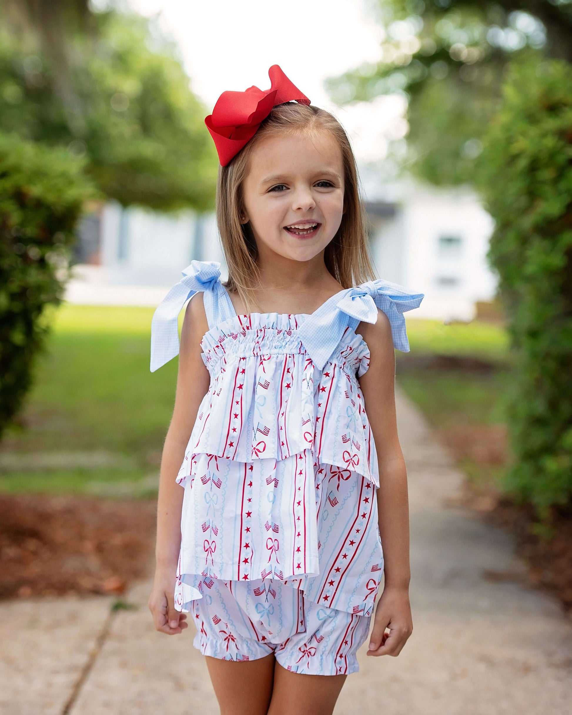 Young girl wearing a light blue and white dress with red accents, standing outdoors.