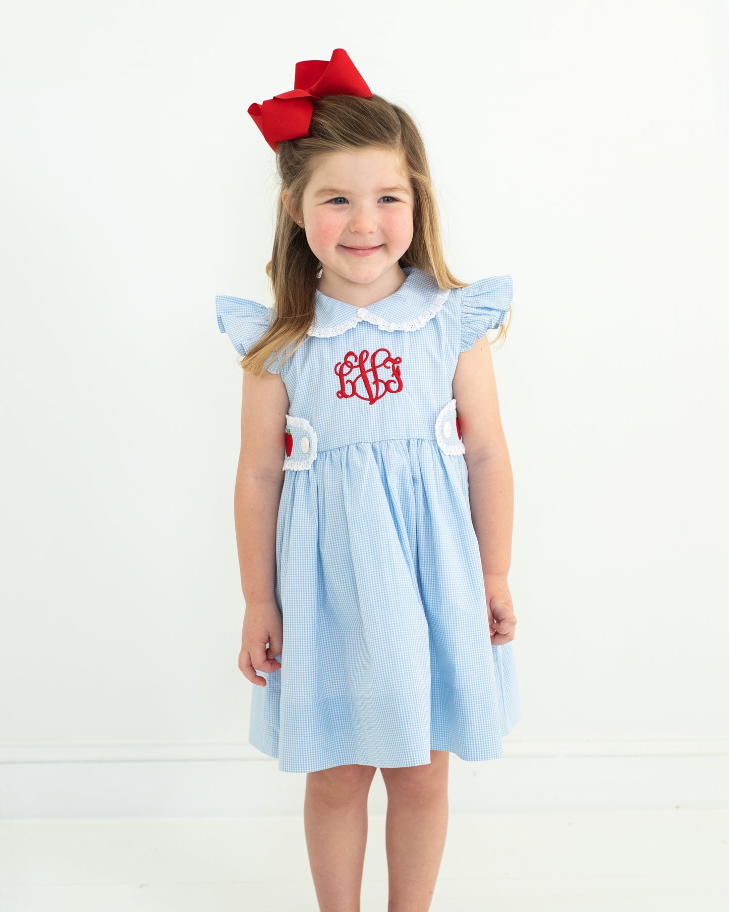 Young girl wearing a light blue dress with a red bow on a white background