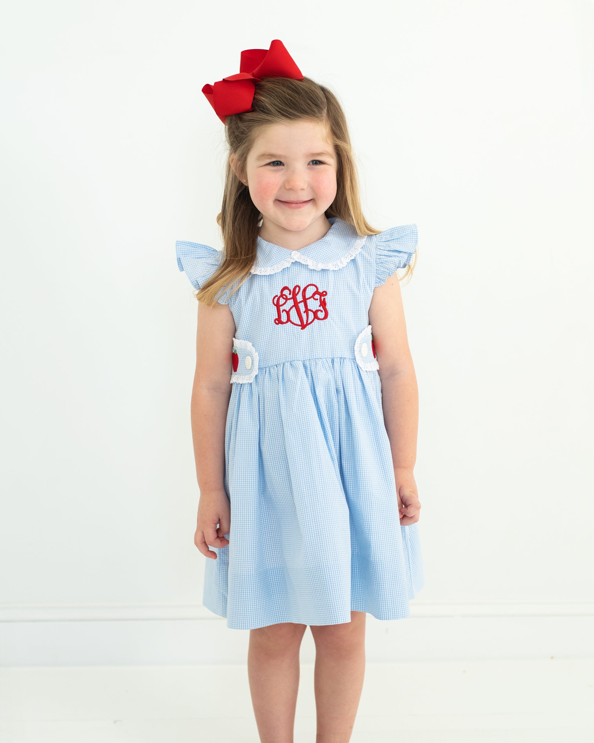 Young girl wearing a light blue dress with a red bow on a white background