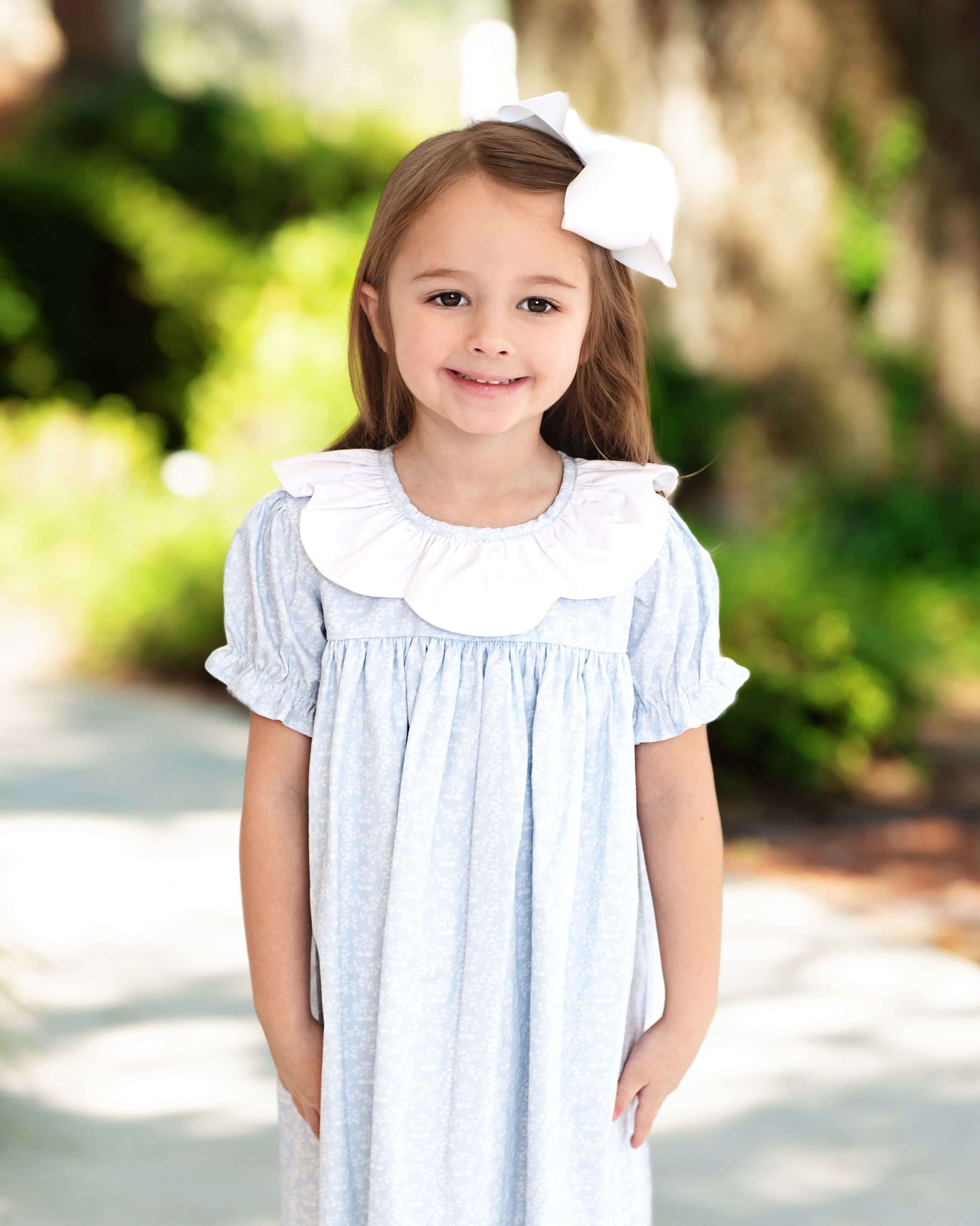 Young girl wearing a light blue dress with a white collar outdoors.