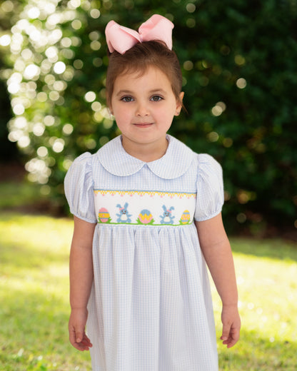 Young girl wearing a light blue dress with bunny and Easter egg design outdoors.