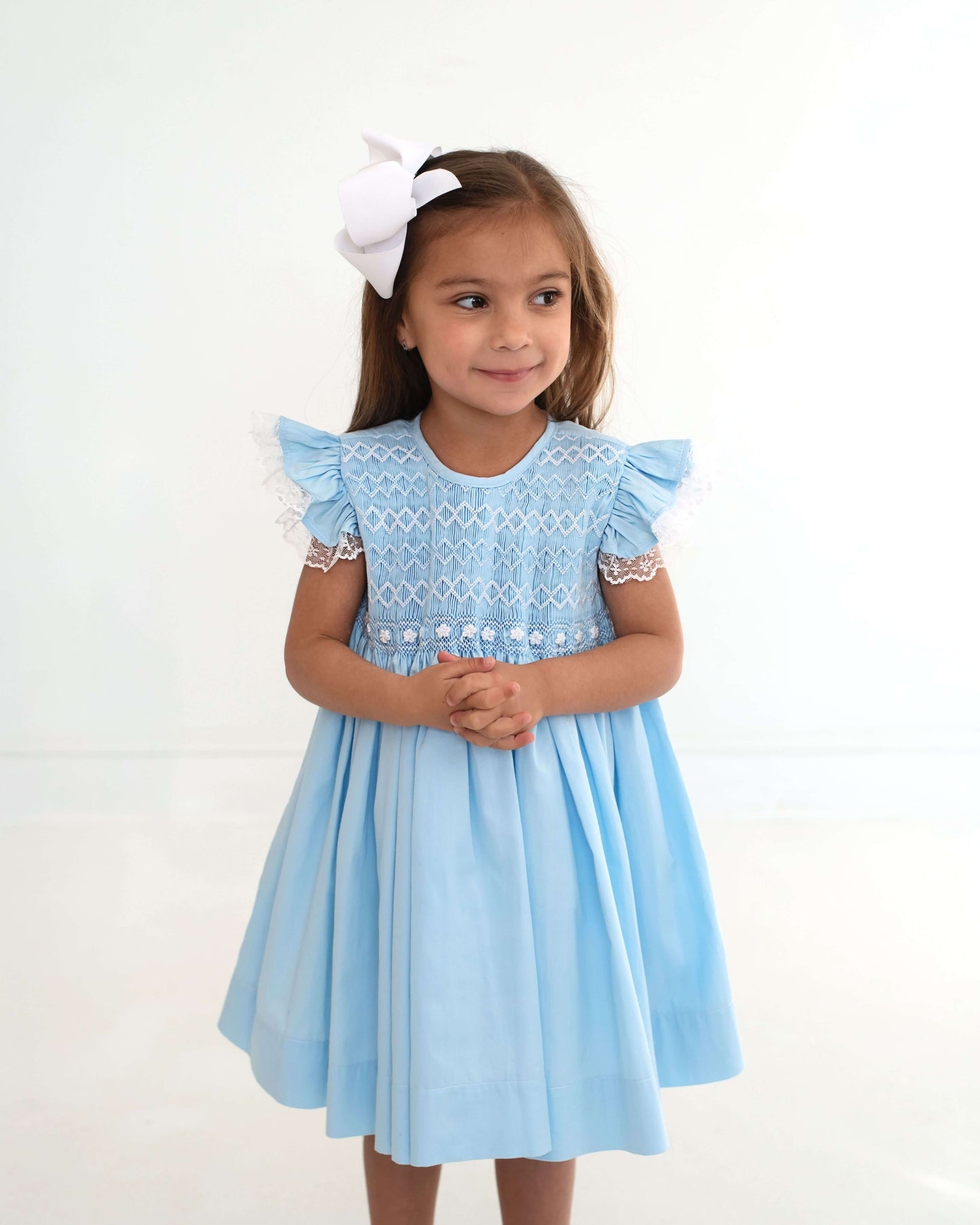 Young girl wearing a light blue dress with lace details on a white background
