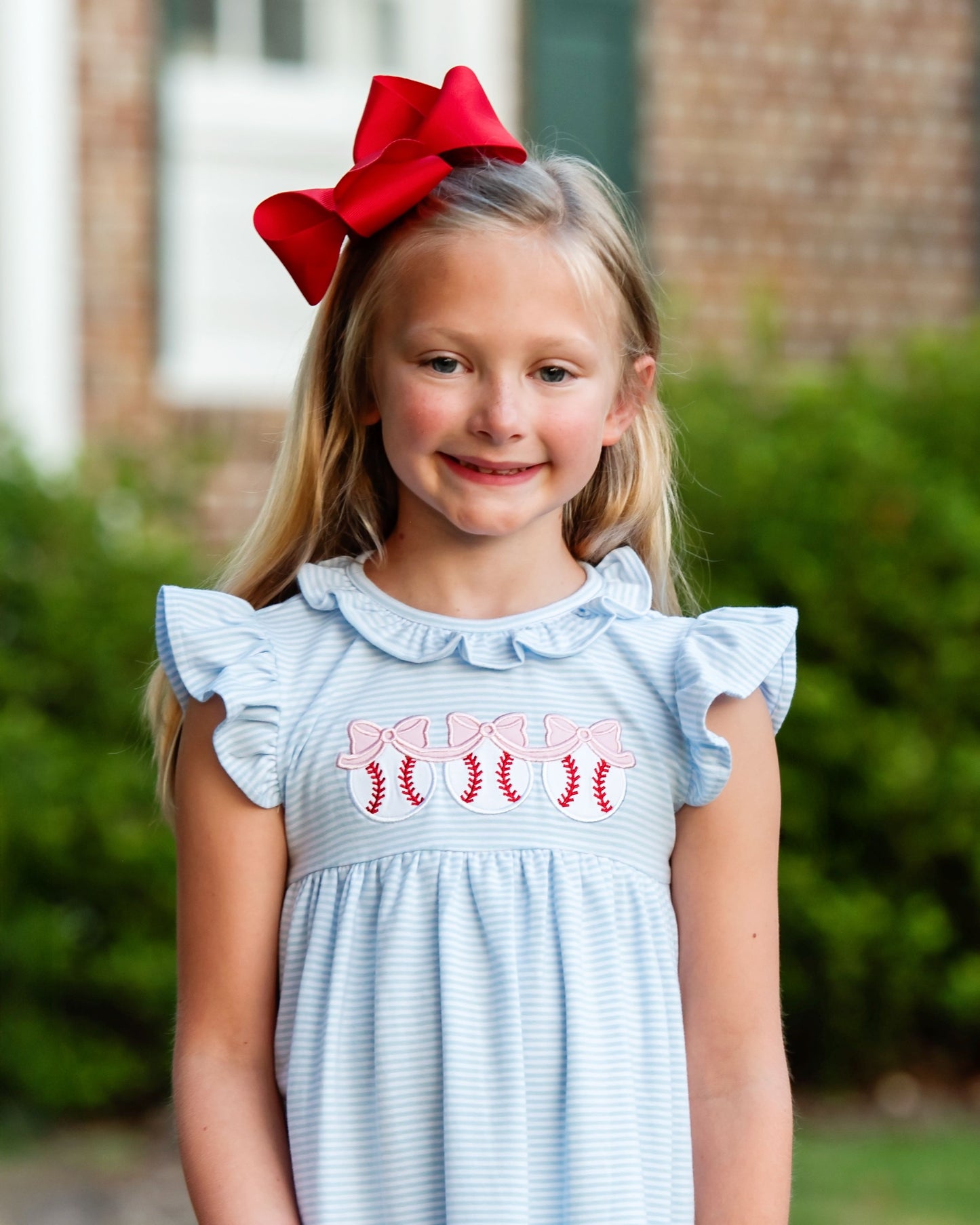 Young girl wearing a light blue dress with red and pink text, standing outdoors.