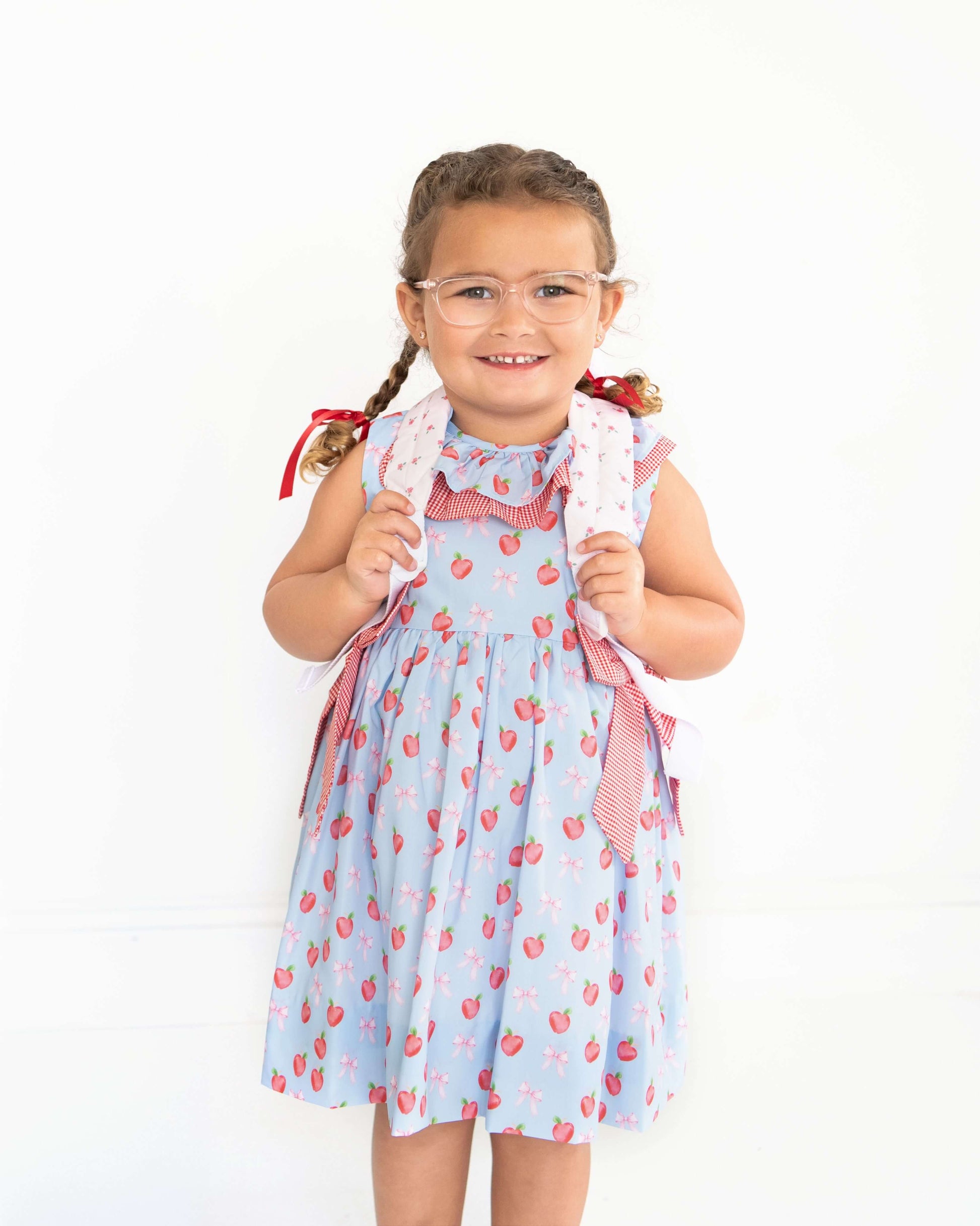 Young girl wearing a light blue dress with red patterns on a white background