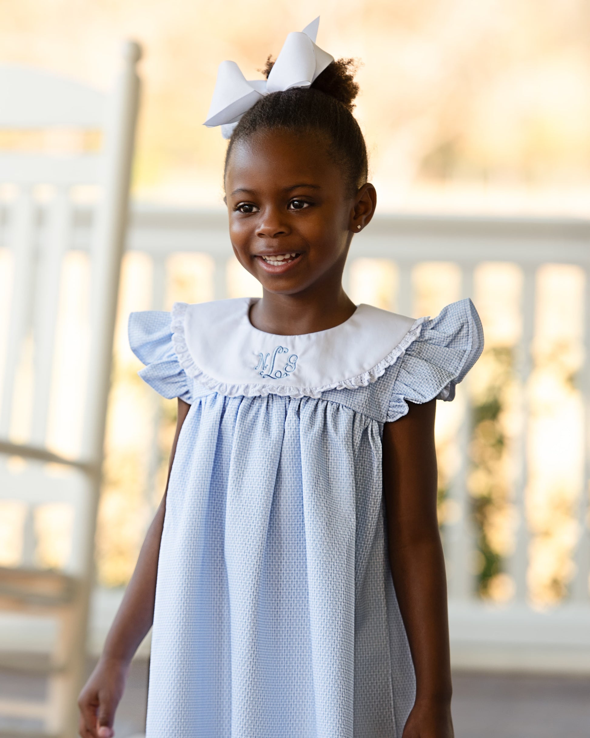 Young girl wearing a light blue dress with white ruffled collar and bow in hair.