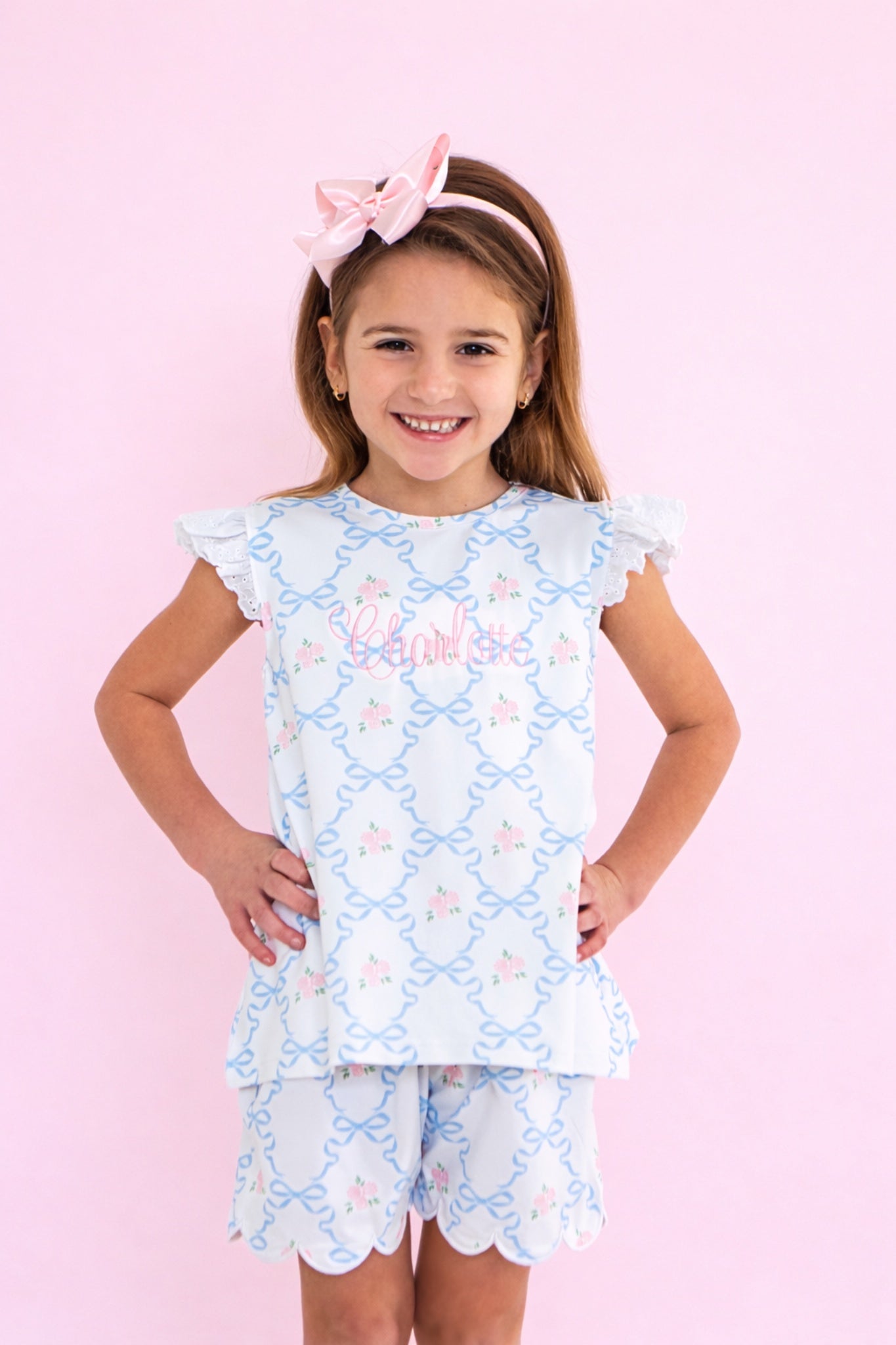 Young girl wearing a light blue play set with floral patterns on a pink background