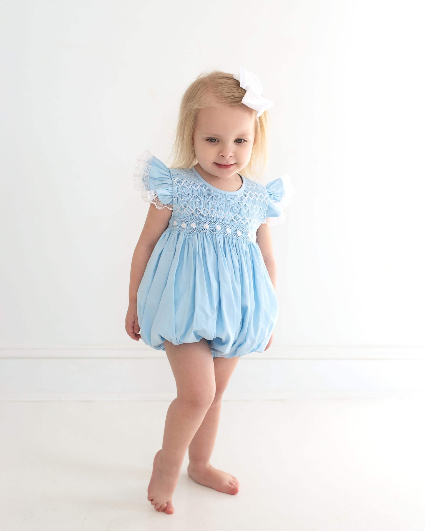Young girl wearing a light blue romper with ruffled sleeves on a white background