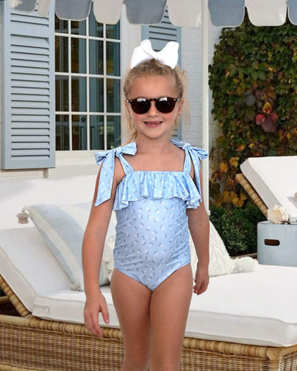Young girl wearing a light blue swimsuit with ruffles and bow straps, standing outdoors.