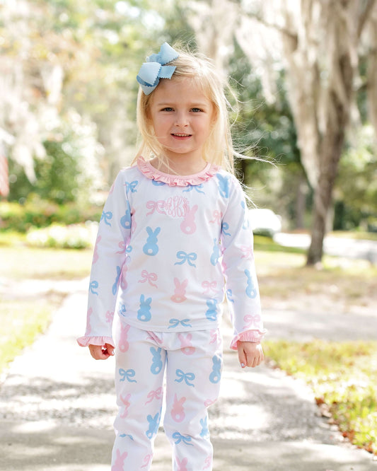 Young girl wearing a pastel bunny and bow patterned outfit outdoors.