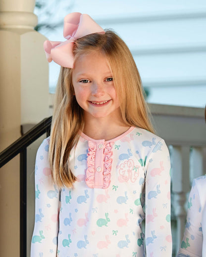 Young girl wearing a pastel floral dress with a large pink bow on her head, standing outdoors.