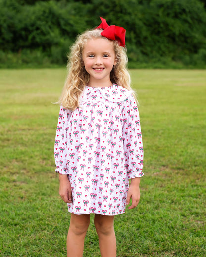 Young girl wearing a patterned dress with a red bow in a grassy field