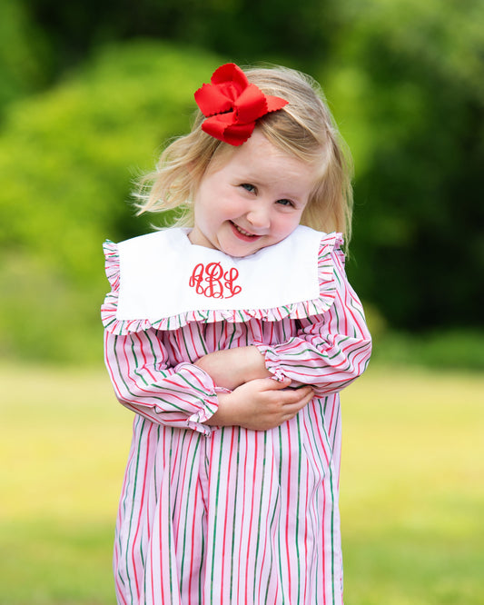 Young girl wearing a pink and white striped dress with a red bow in her hair, standing outdoors.