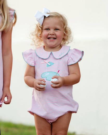 Young girl wearing a pink and white striped swimsuit with a cloud design, standing outdoors.