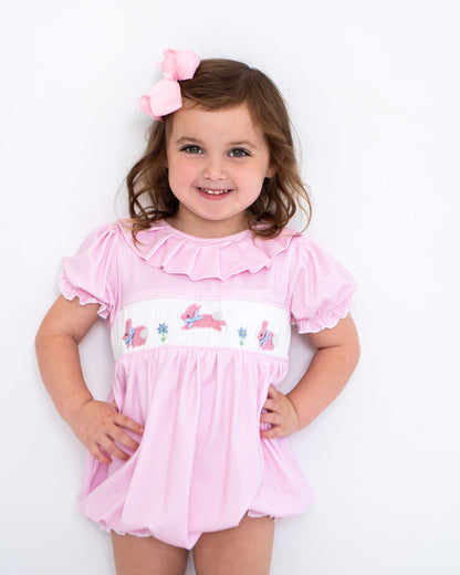 Young girl wearing a pink bubble with smocked bunnies on a white background