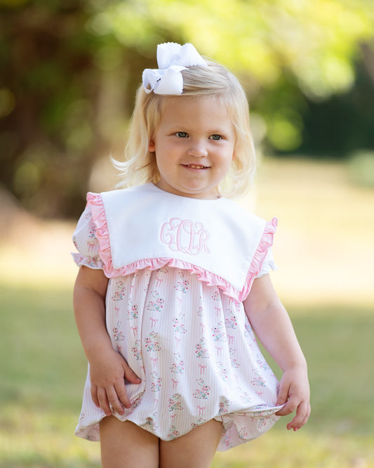 Young girl wearing a pink bunny bubble with pink trim and a large bow in her hair, standing outdoors.