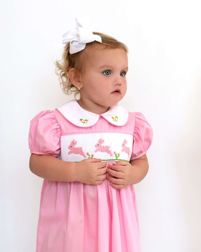 Young girl wearing a pink dress with a white collar and bunny design on a plain background
