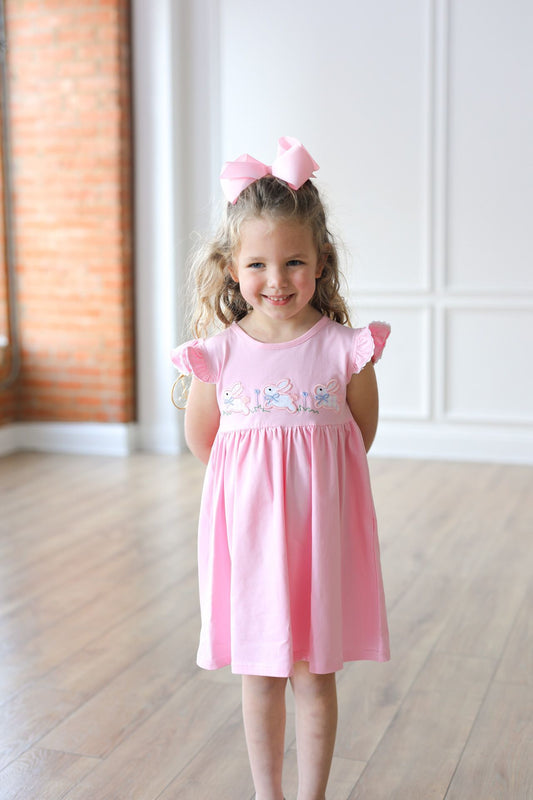Young girl wearing a pink dress with butterfly sleeves in a bright room.