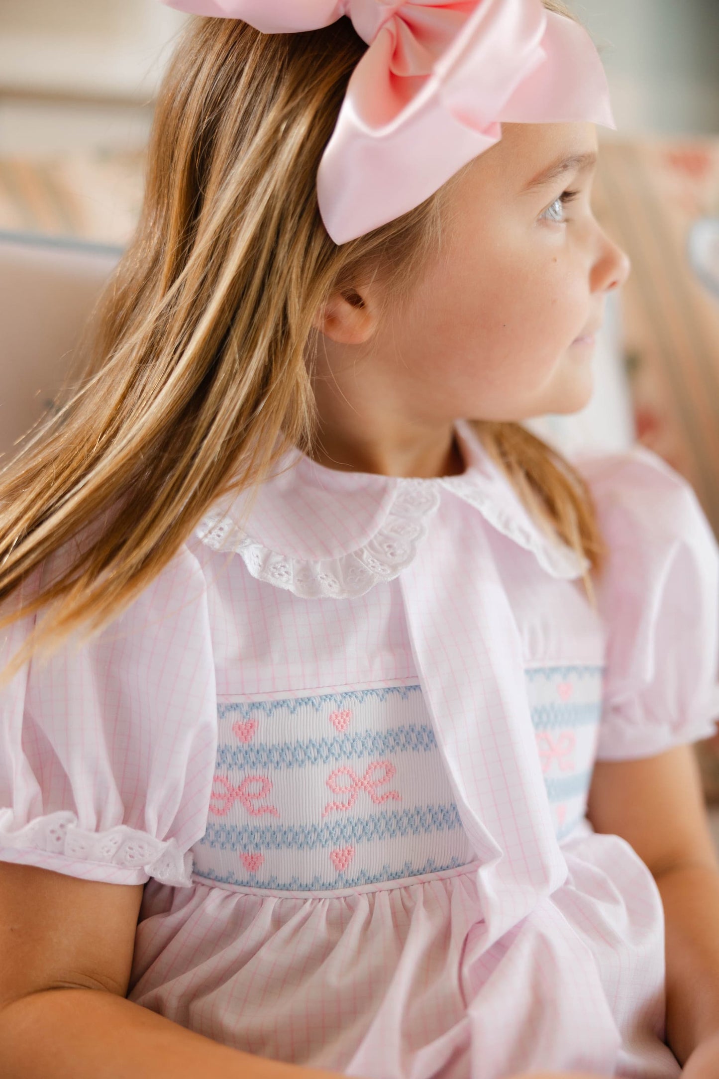 Young girl wearing a pink dress with floral embroidery and a matching headband.