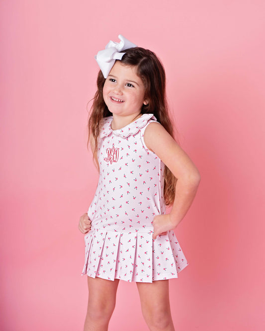 Young girl wearing a pink dress with white polka dots and a white bow against a pink background