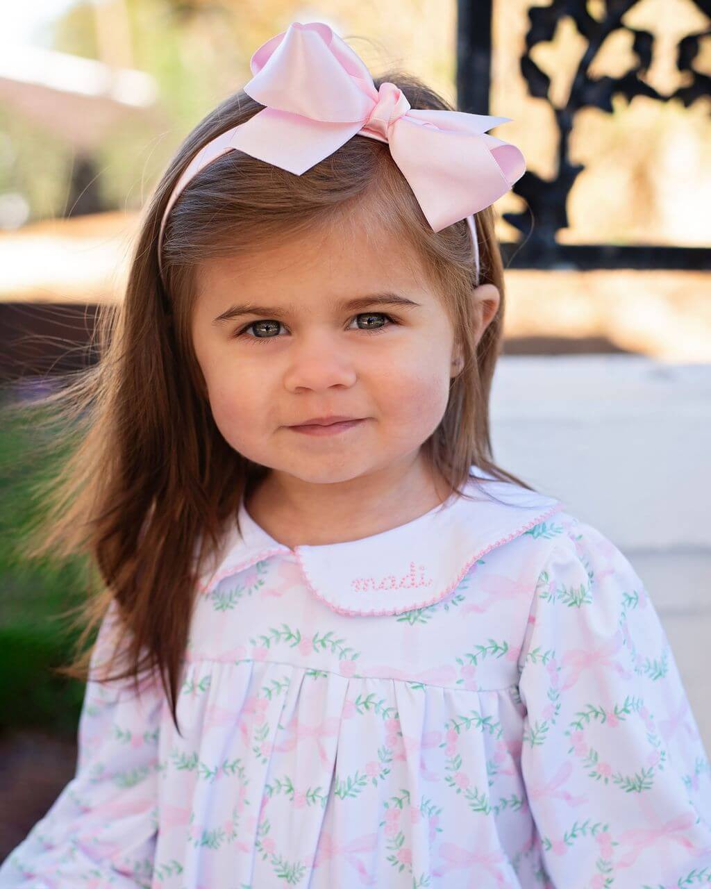 Young girl wearing a pink floral dress and headband with a large bow.