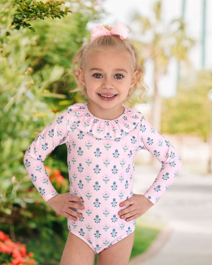 Young girl wearing a pink floral swimsuit with long sleeves outdoors.