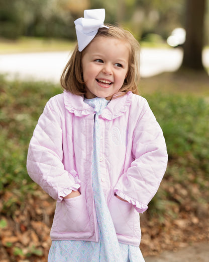 Young girl wearing a pink jacket with a large white bow in her hair, standing outdoors.