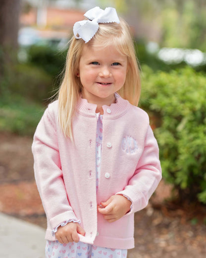 Young girl wearing a pink jacket with a white bow in her hair, standing outdoors.