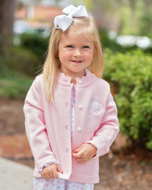 Young girl wearing a pink jacket with a white bow in her hair, standing outdoors.