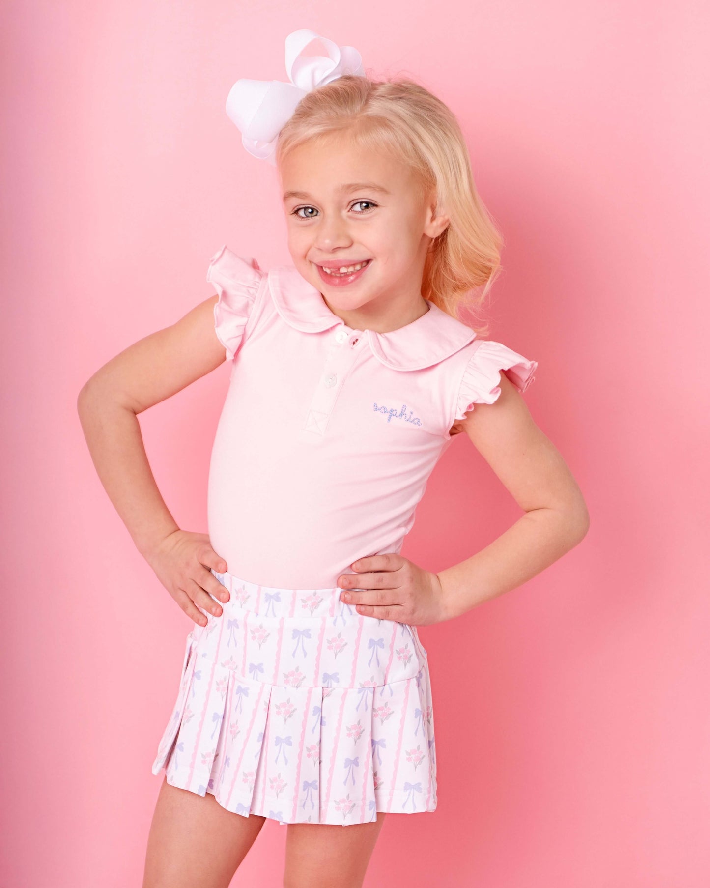 Young girl wearing a pink outfit with a white bow on a pink background