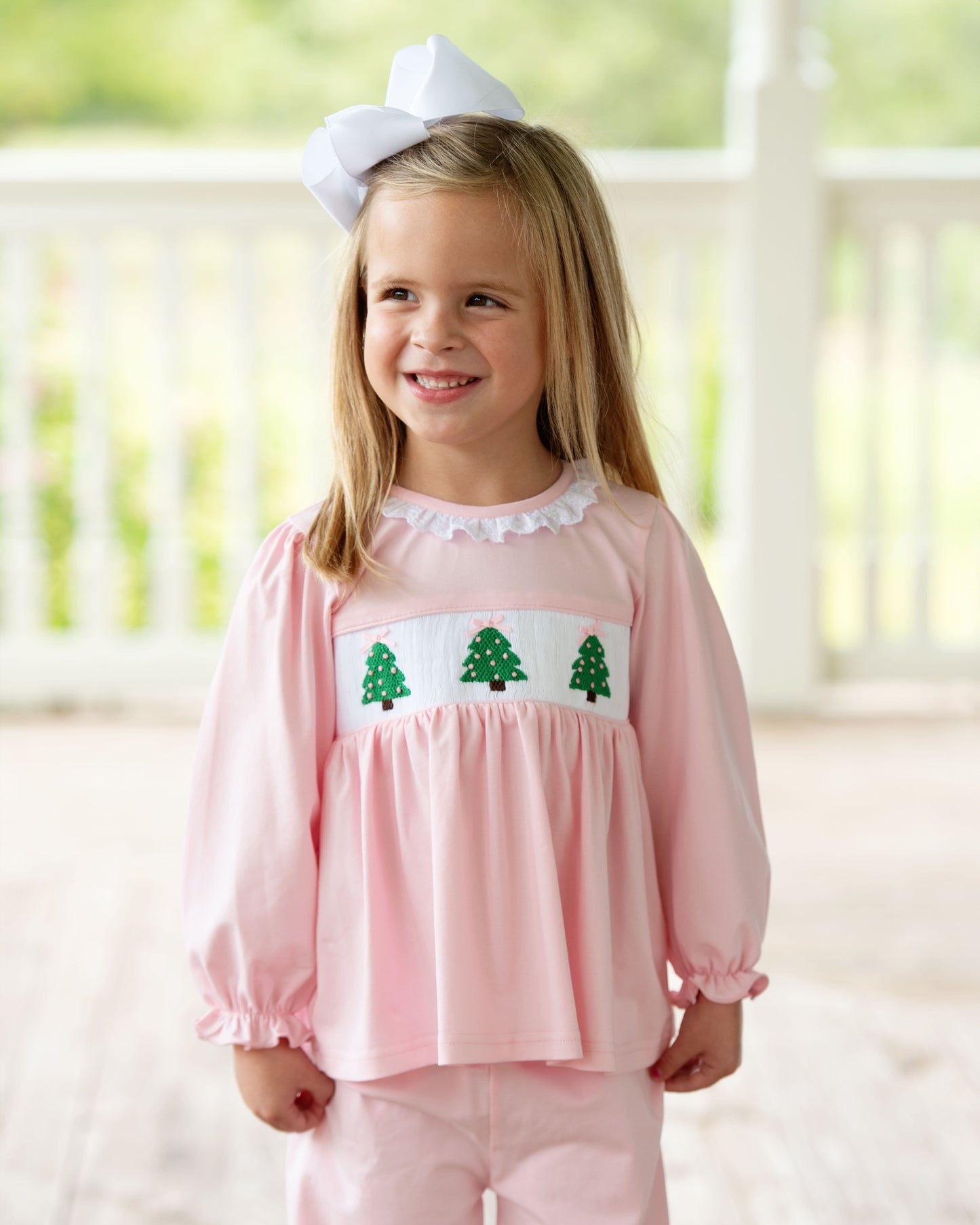 Young girl wearing a pink outfit with green tree designs in a bright room.