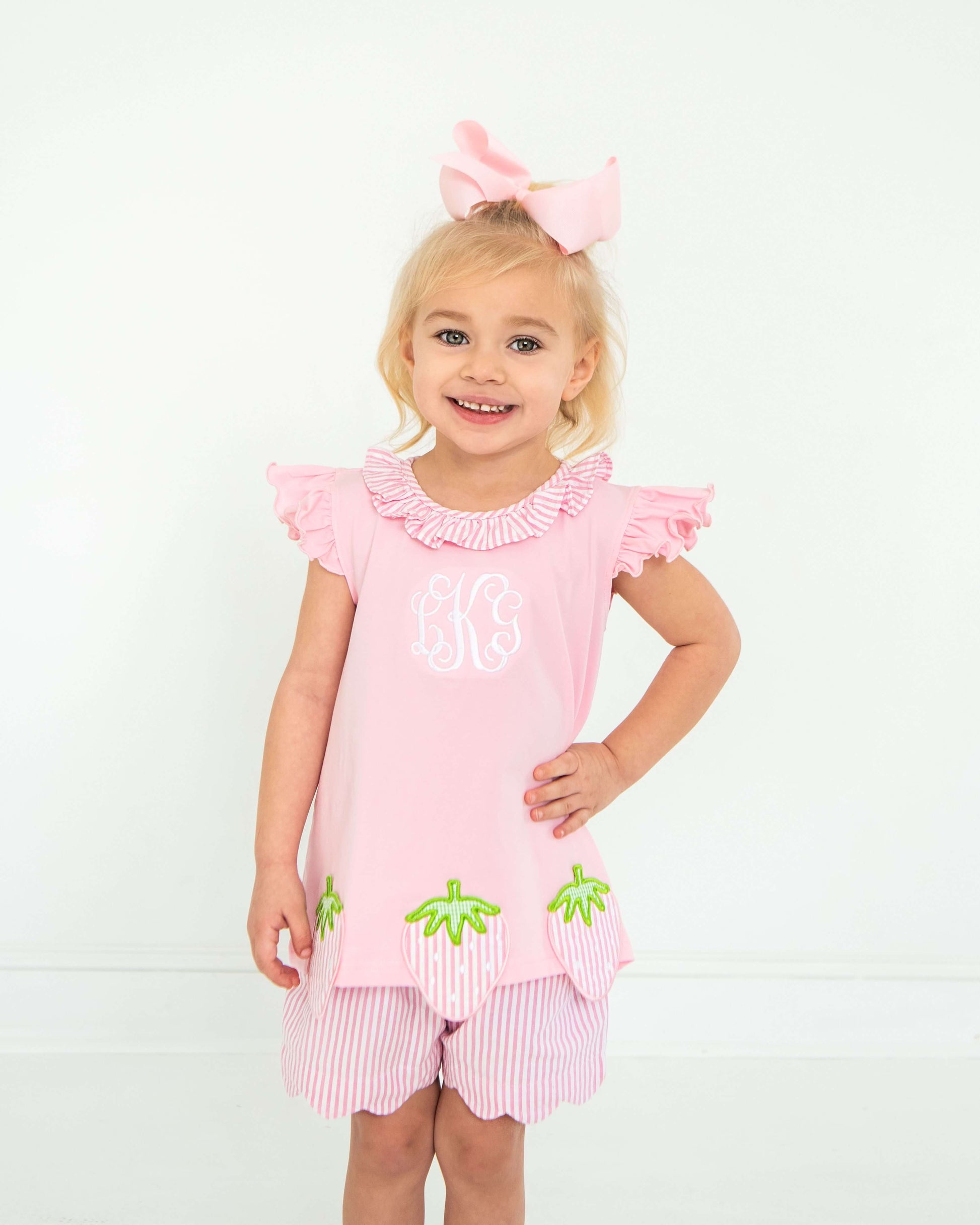 Young girl wearing a pink outfit with ruffled sleeves and green accents on a white background