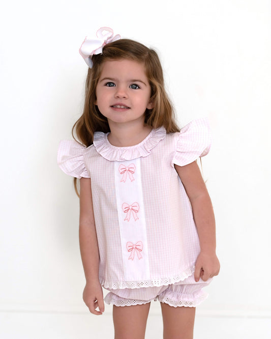 Young girl wearing a pink outfit with ruffles and bows on a white background