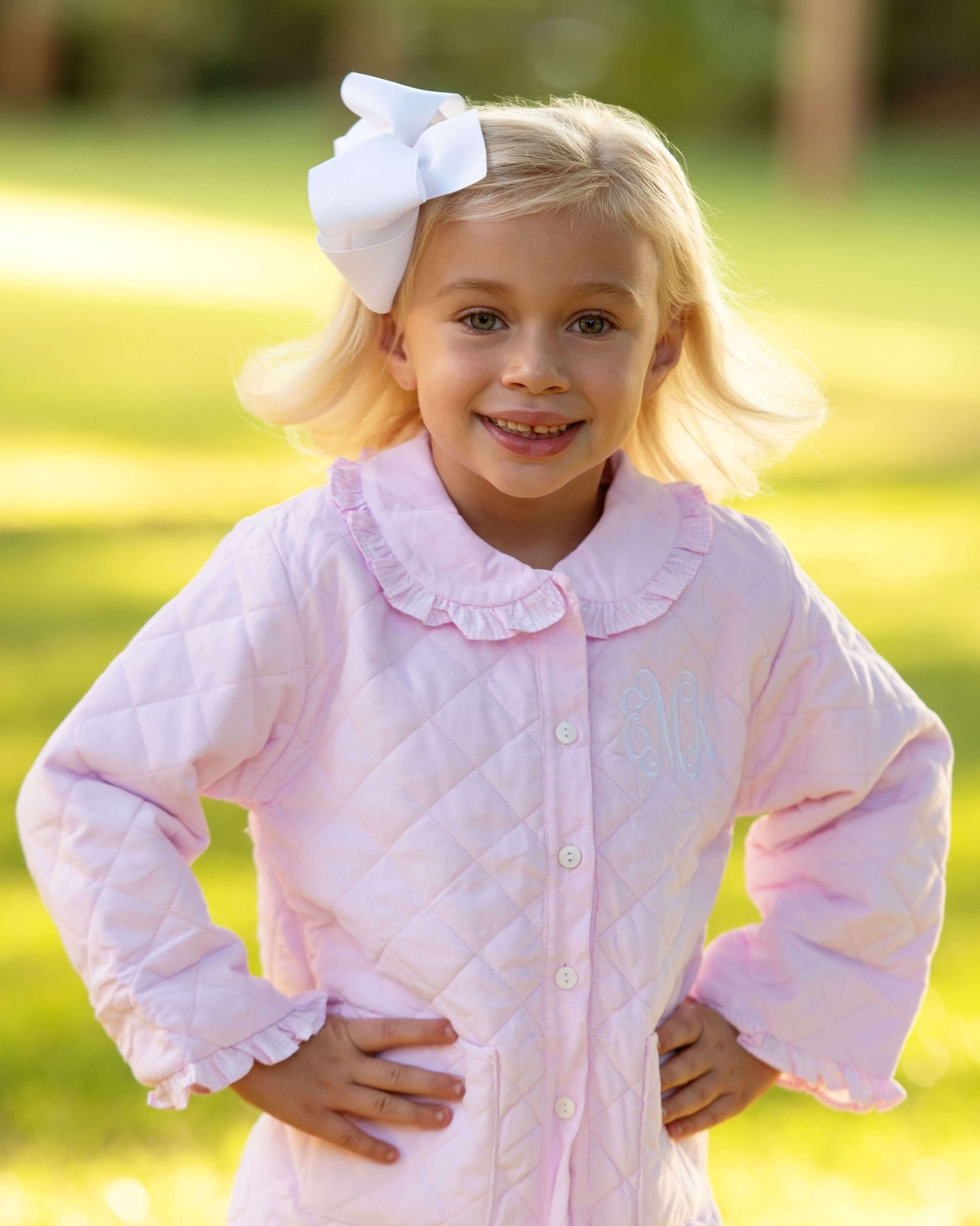 Young girl wearing a pink quilted jacket with a white bow outdoors.