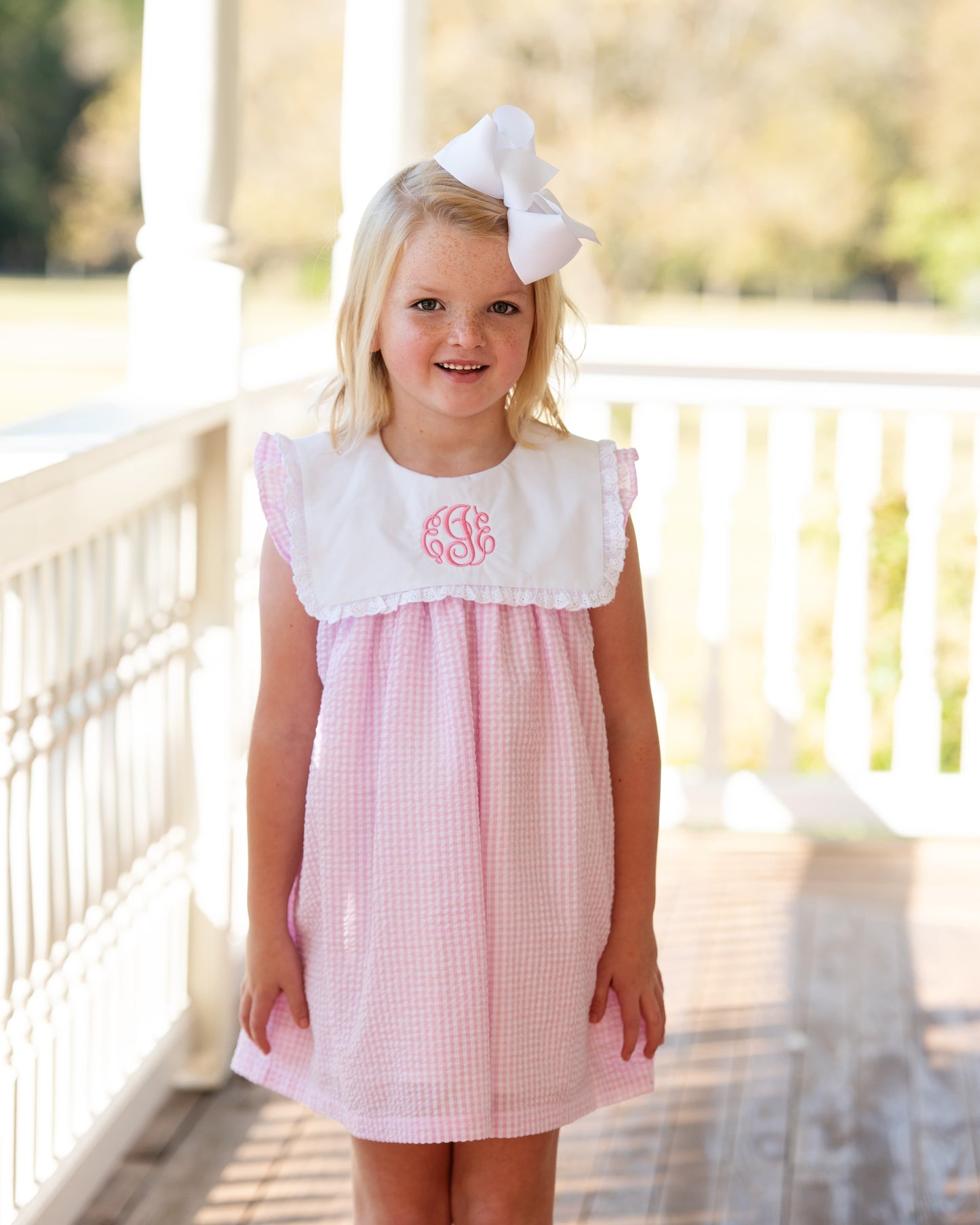 Young girl wearing a pink seersucker dress with white lace details on a porch.