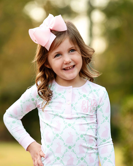 Young girl wearing a pink shirt with a floral pattern and a large pink bow in her hair, standing outdoors.