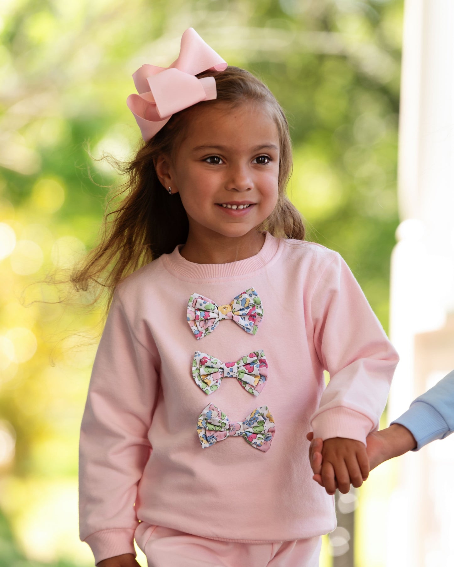 Young girl wearing a pink sweatshirt with floral bow designs outdoors