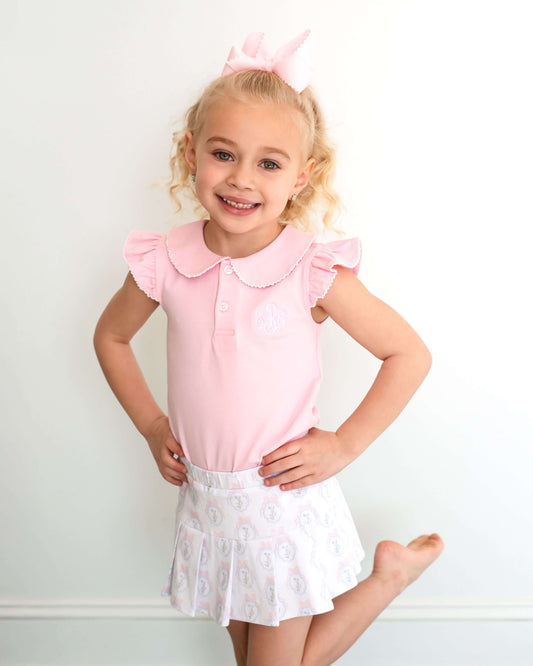 Young girl wearing a pink top and white skirt with a plain background